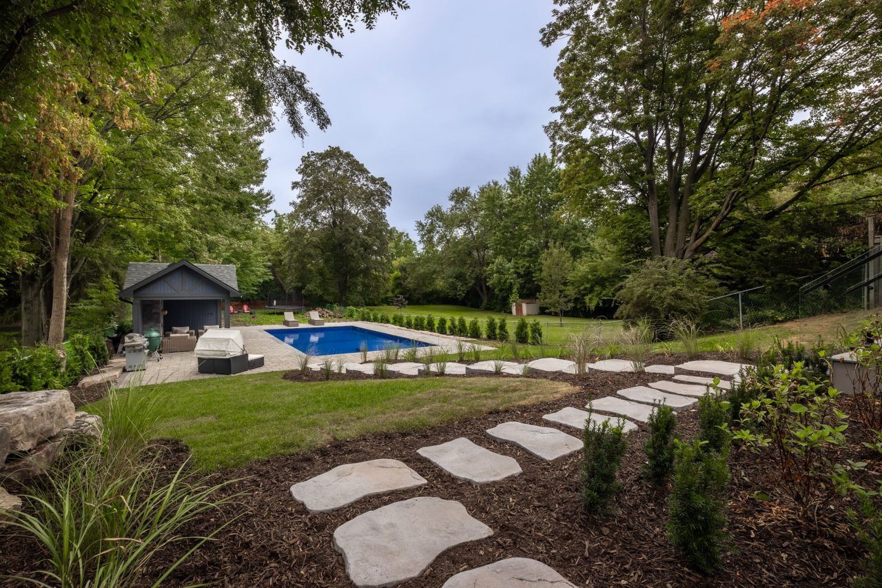 Backyard with a pool and pergola covering a seated area.