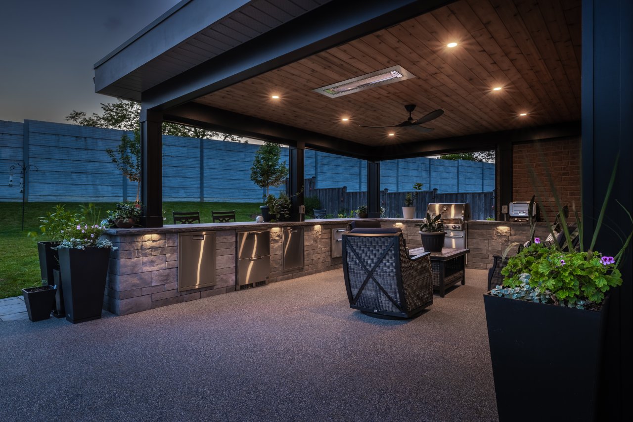 Covered outdoor kitchen and lounge designed for entertaining, with integrated lighting, built-in appliances, and defined seating areas