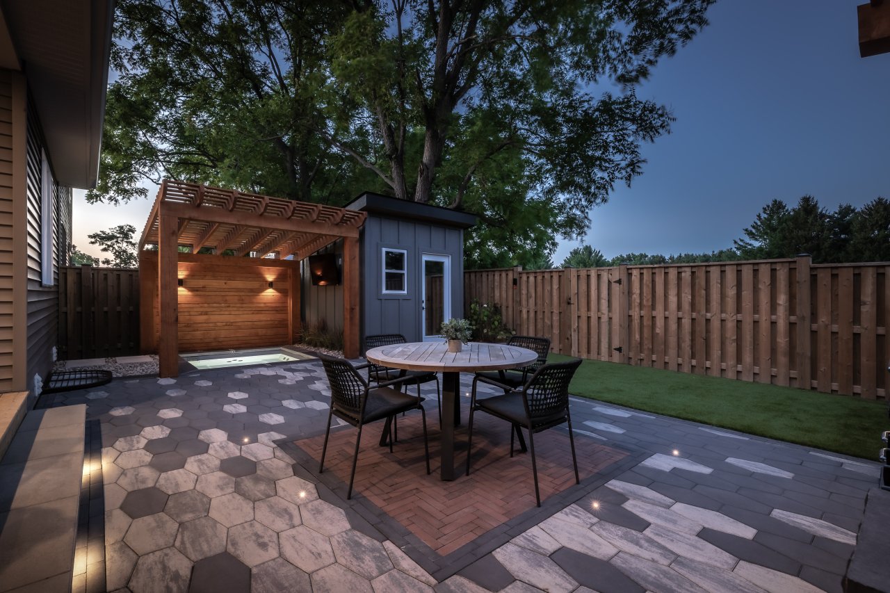Backyard landscape design featuring a pergola-covered spa, dining area, and cohesive paver layout with integrated lighting