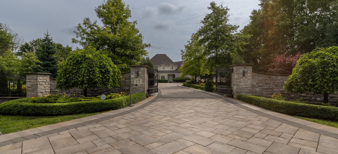 Residential property with a large paver stone driveway surrounded by landscapes hedges and trees