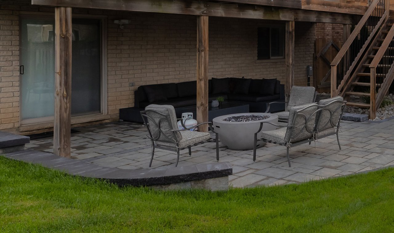 Close up of residential backyard paver patio with healthy mowed grass and seating around a fire pit