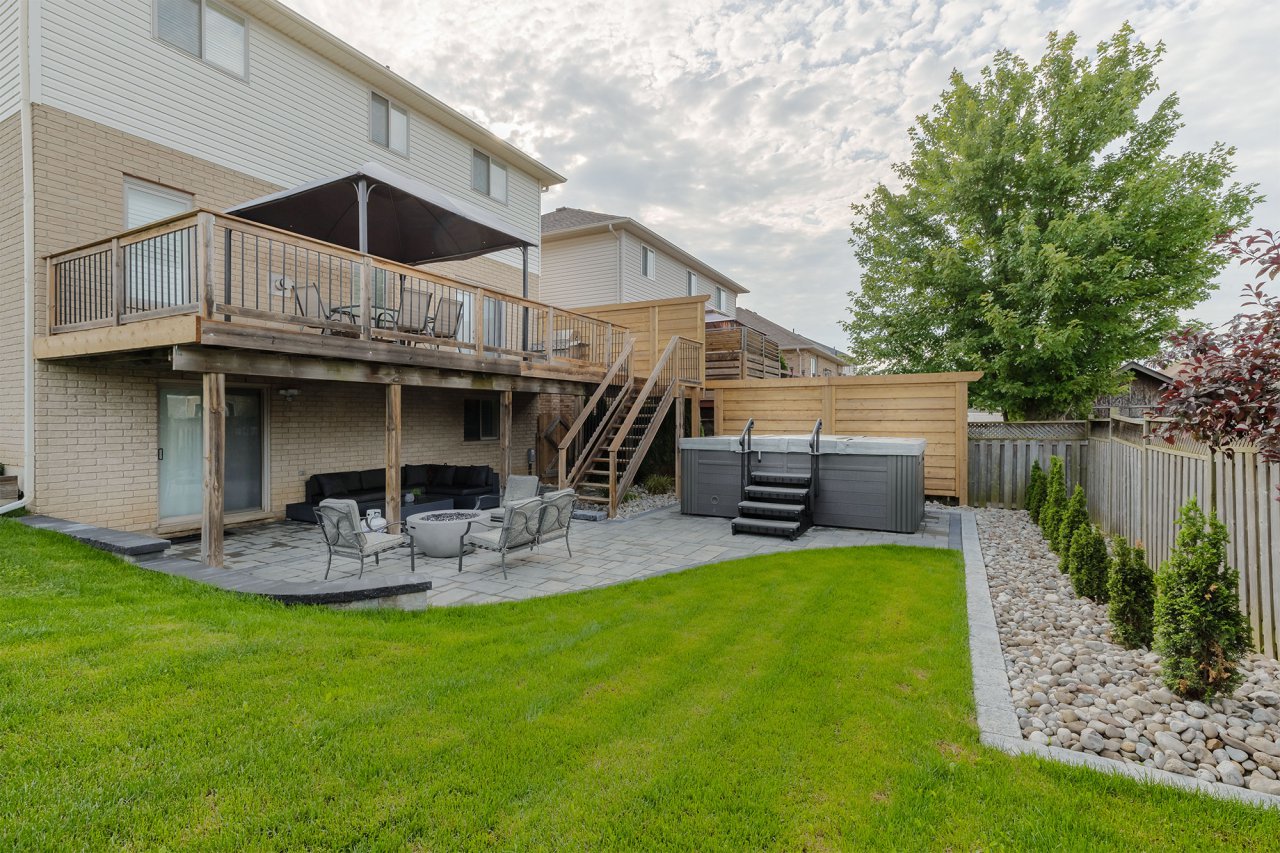 Residential backyard landscaped with wood deck, patio, hot tub, fire pit, mowed lawn and rock garden.