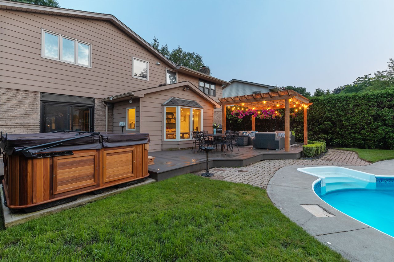 Residential backyard with a hottub, patio, pergola with twinkling lights, a pool and privacy hedges