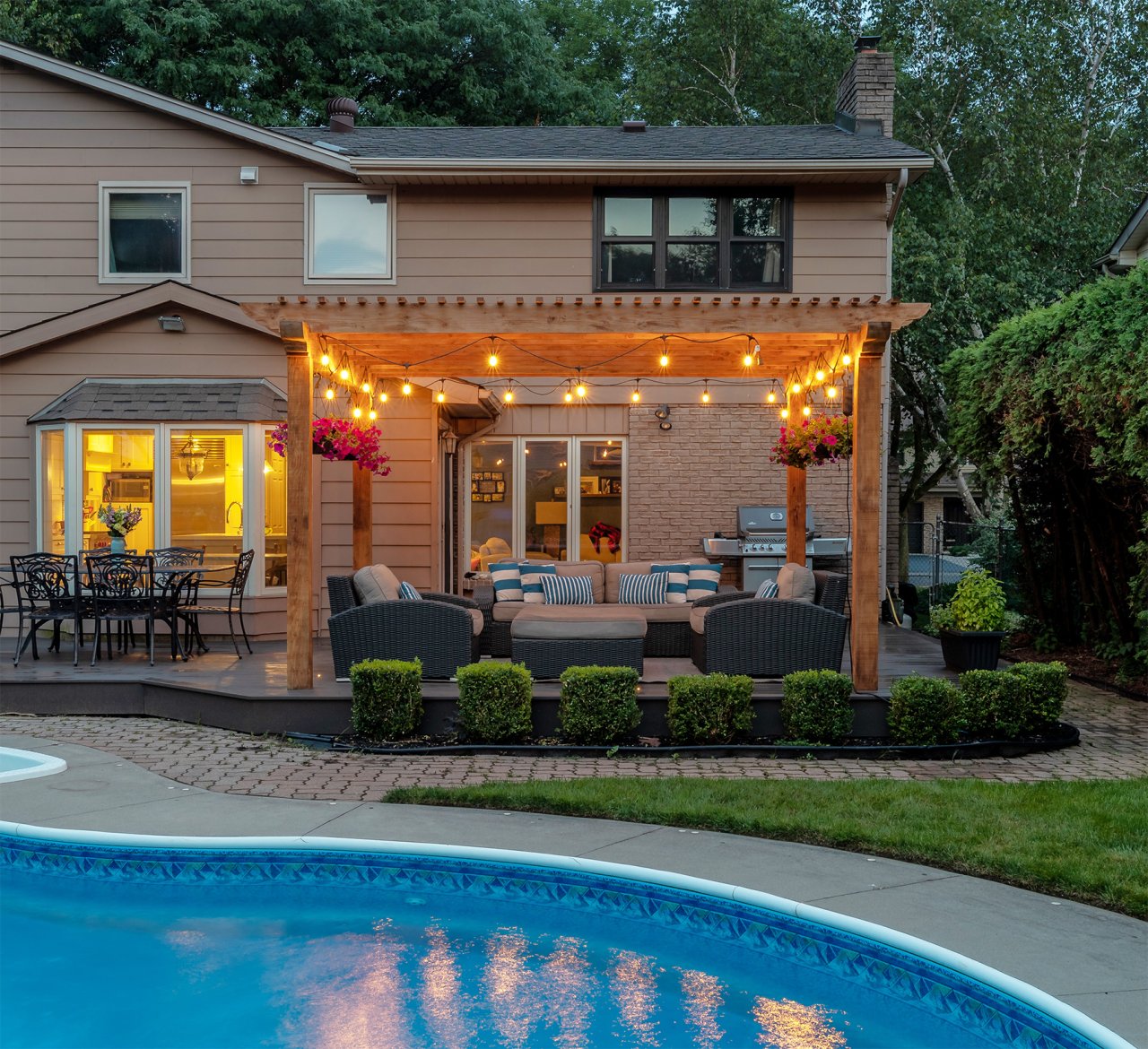 Residential backyard with patio and pergola with twinkling lights and hanging flower baskets