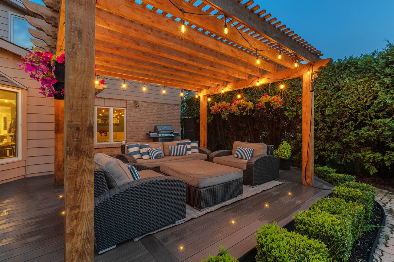 Residential backyard patio with a pergola with twinkling lights and hanging flower baskets