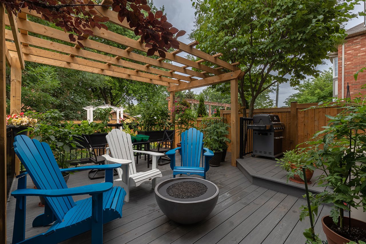 Backyard patio with large arbour and chairs around a fire pit.